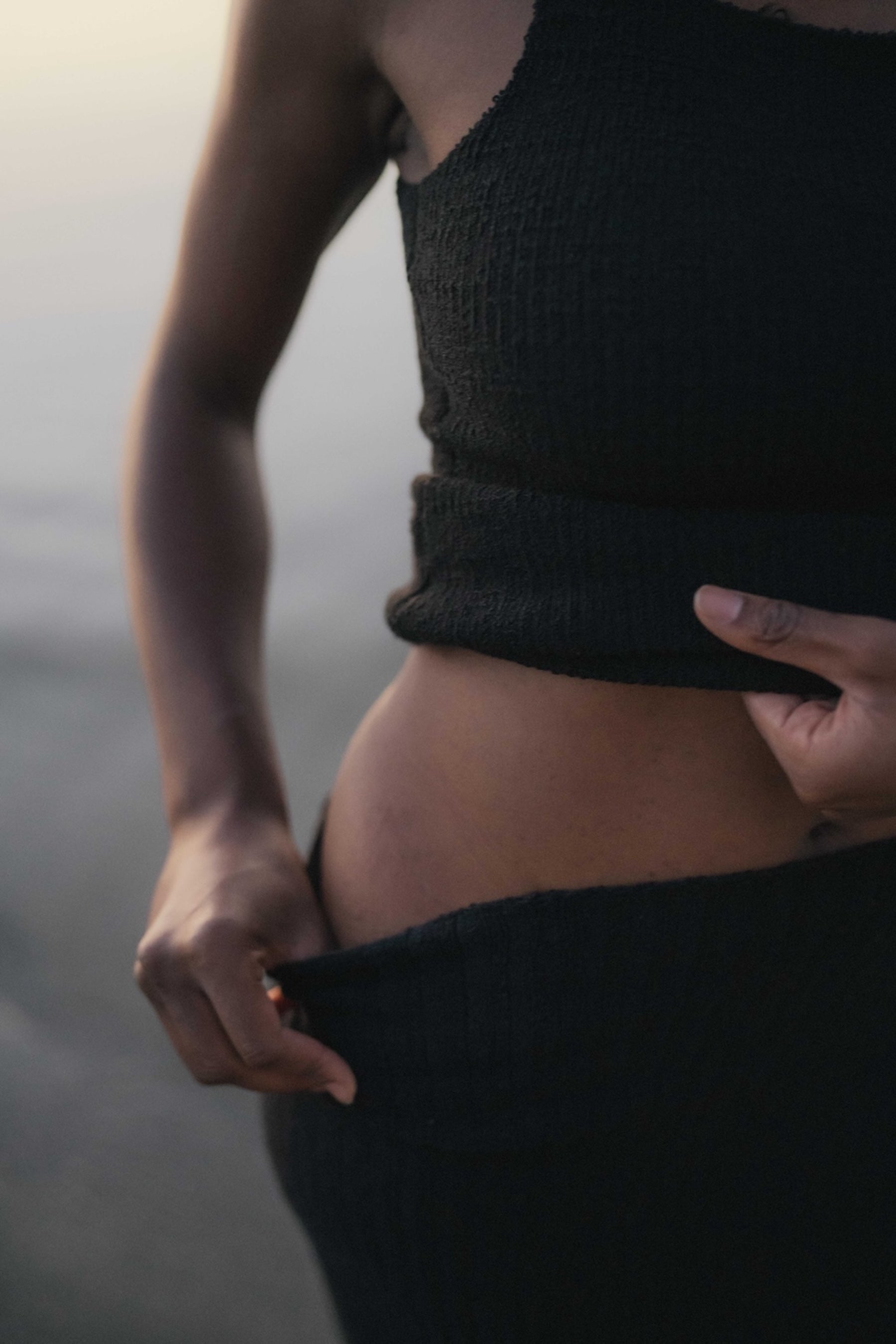 Person wearing a black sleeveless top and pants against a skirt background