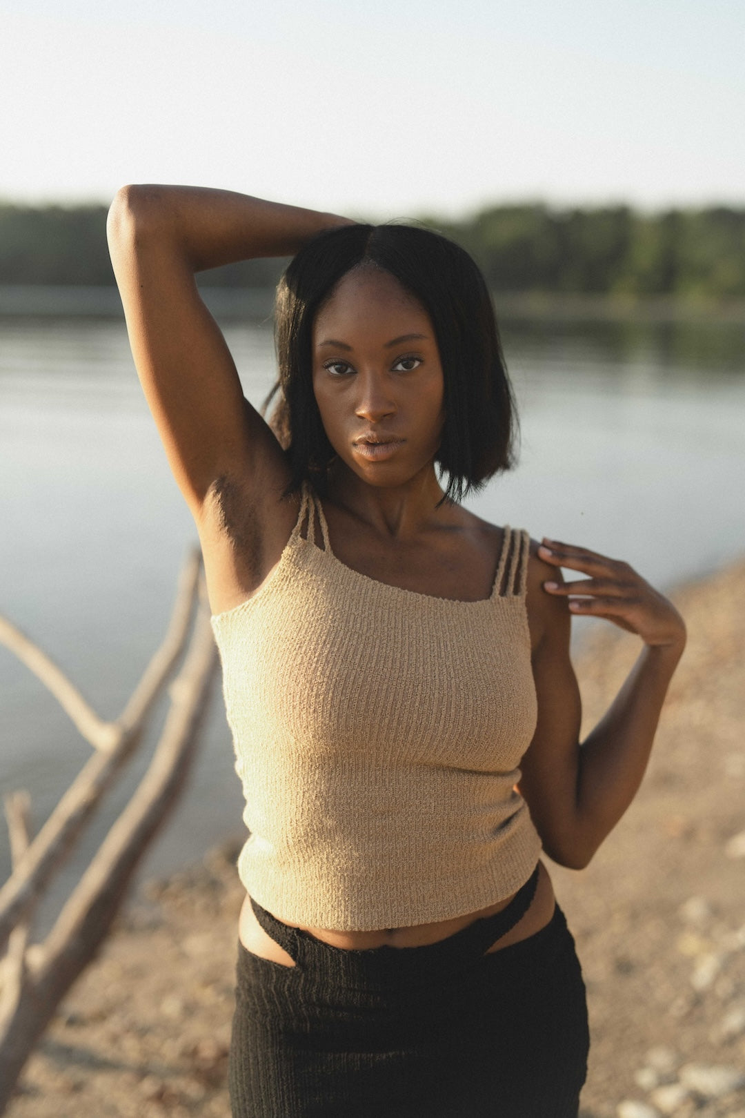 Woman posing by a lake wearing a beige knit tank top