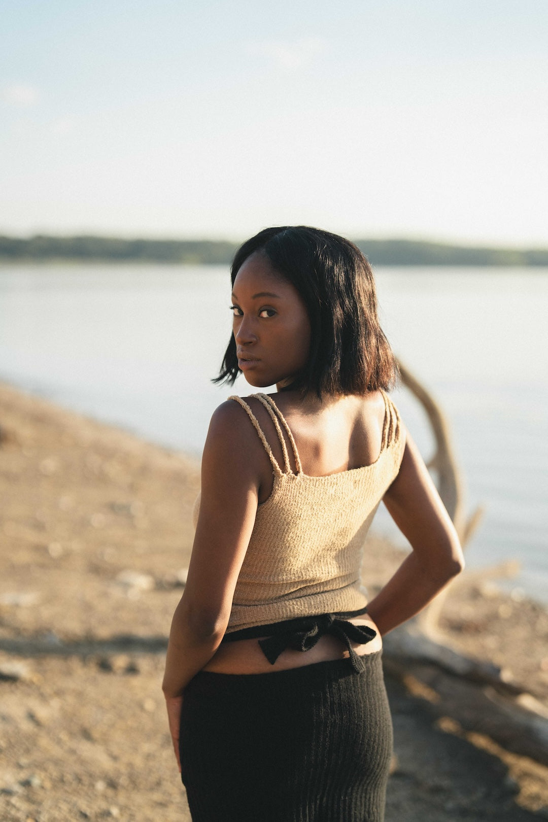 Woman posing by a lake wearing a beige knit tank top