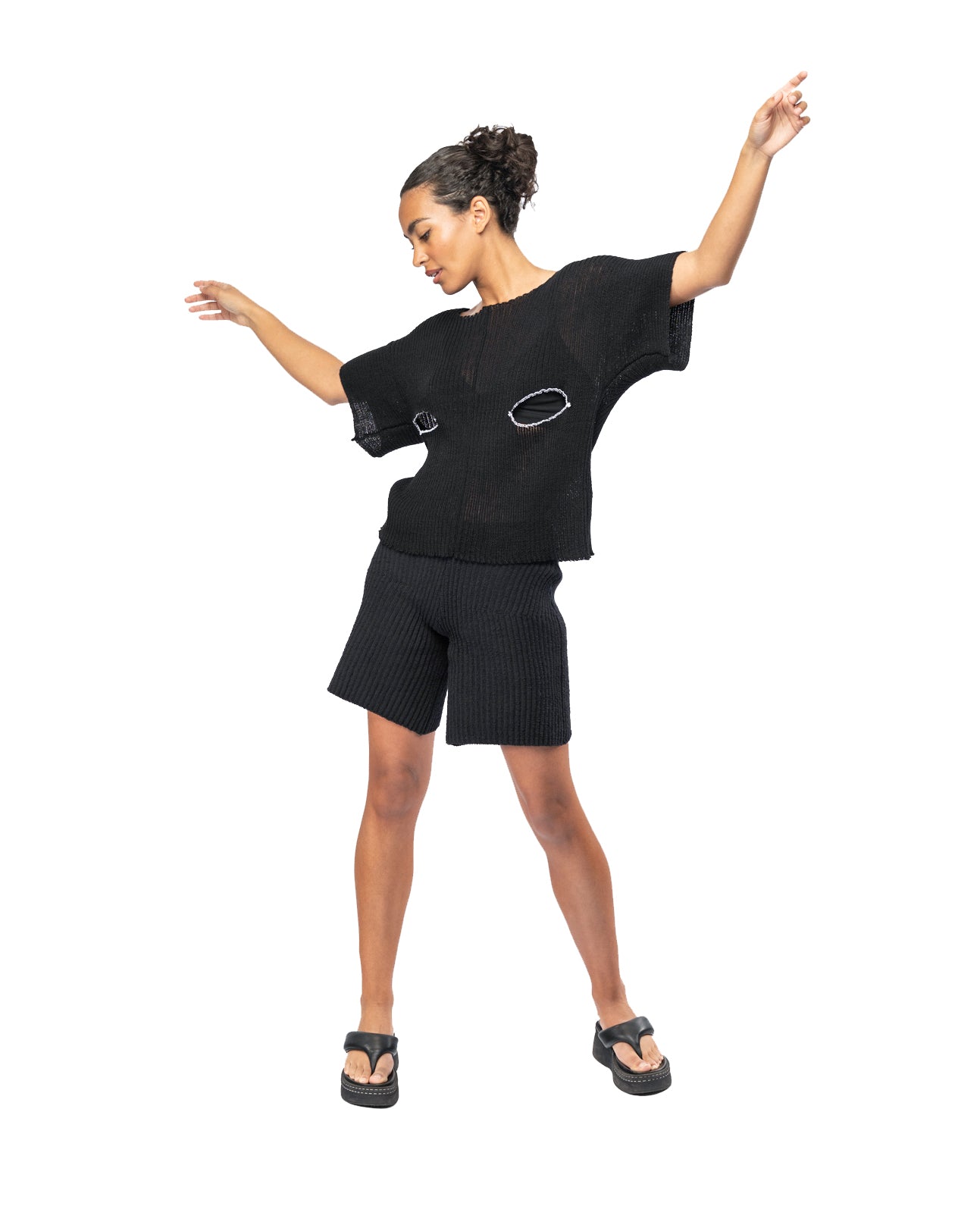 Woman wearing a black knit outfit with open arms on a white background
