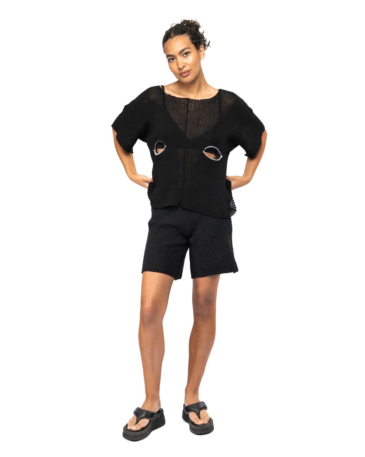 Woman wearing a black knit outfit with cut-out details on a white background
