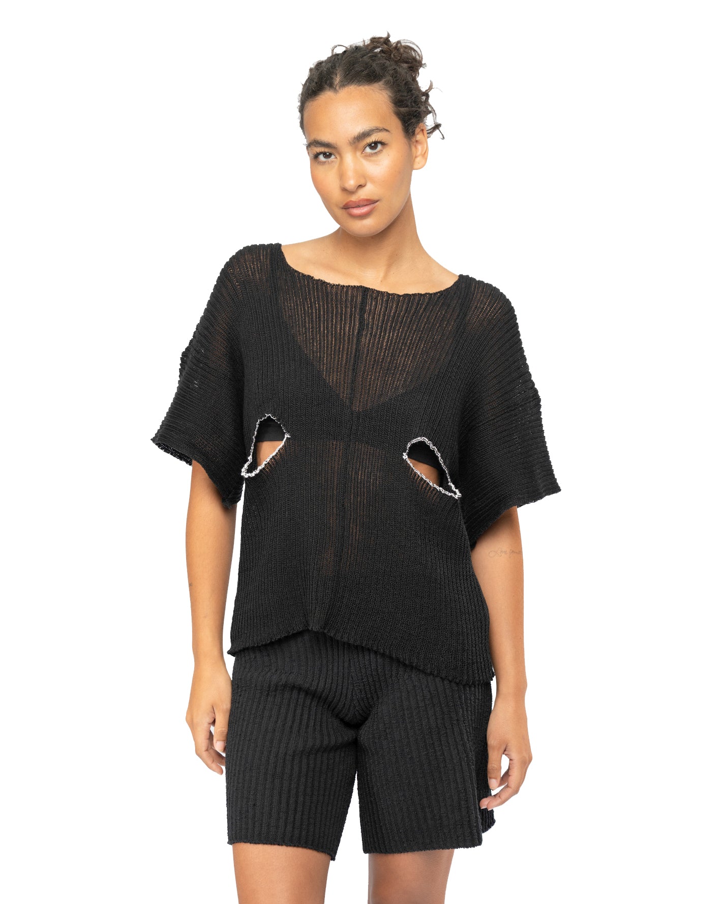 Woman wearing a black knit outfit with cut-out details on a white background