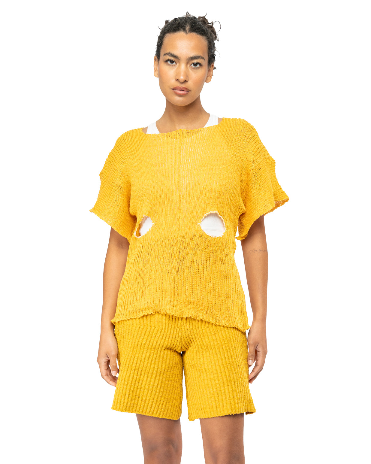 Woman wearing a knit yellow ribbed outfit with cut-out details on a white background
