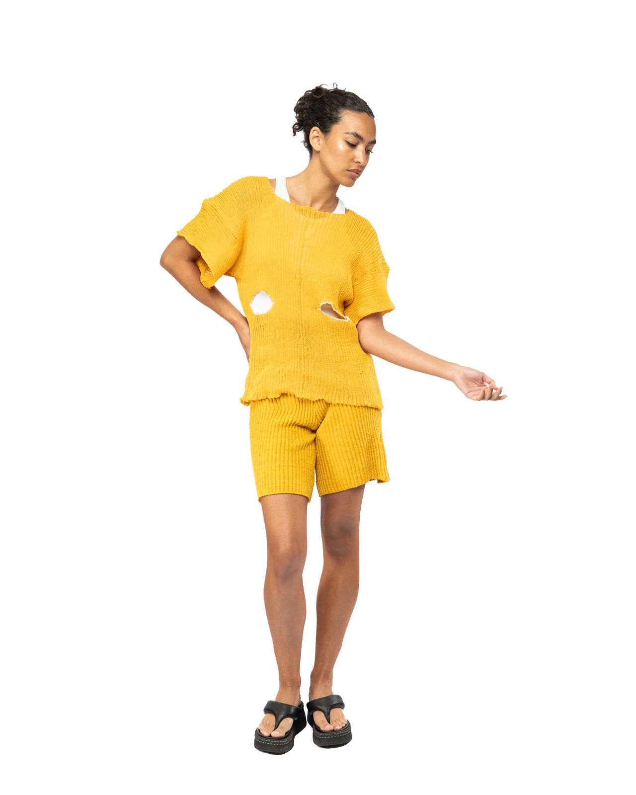 Woman wearing a knit yellow ribbed outfit with cut-out details on a white background